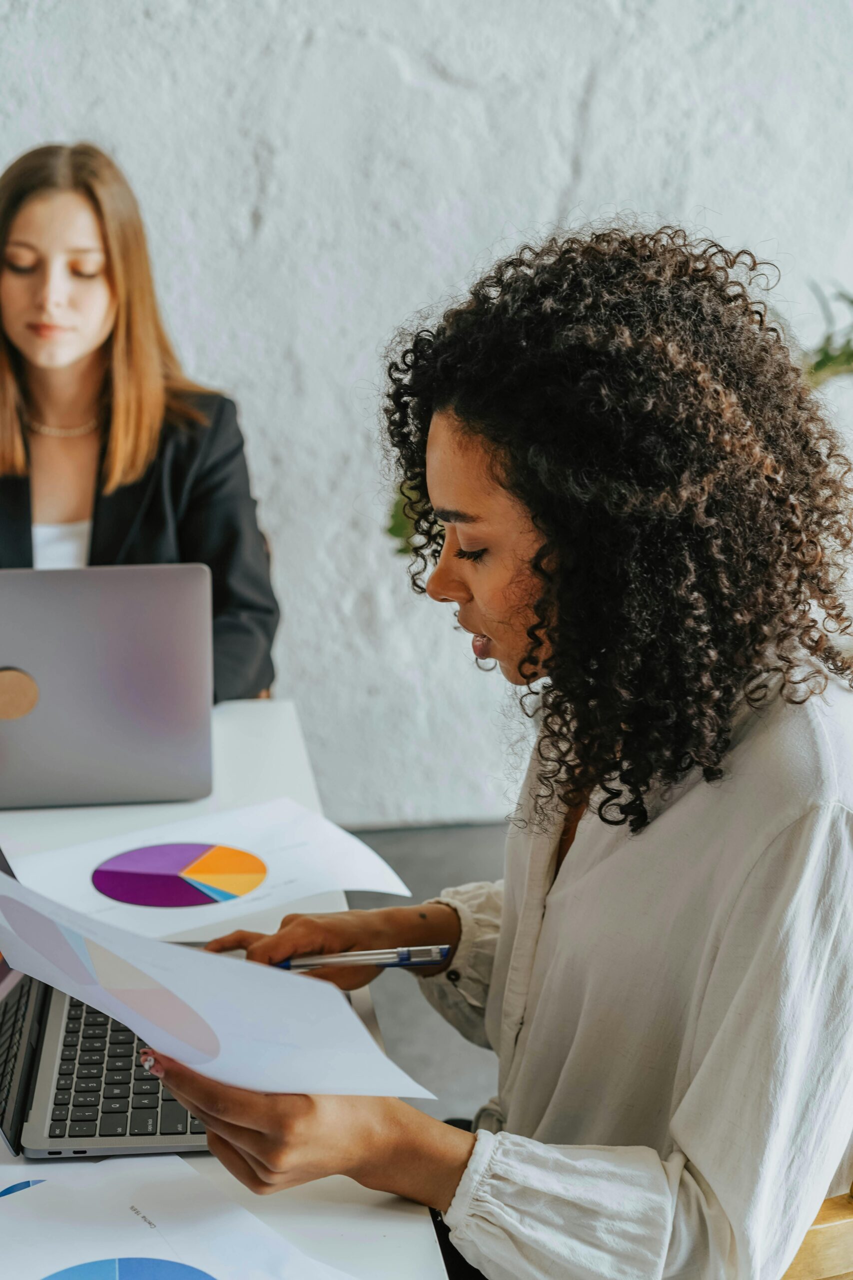 Two women focused on analyzing business graphs in a modern office setting.